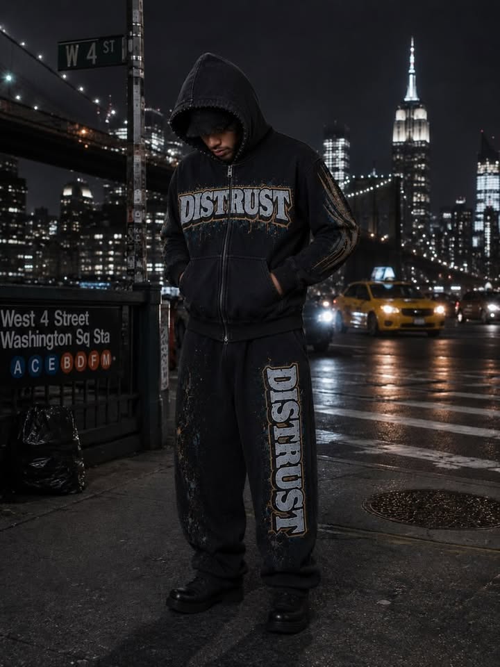 Distrust model wearing oversized blacked-out streetwear on a NYC street at night